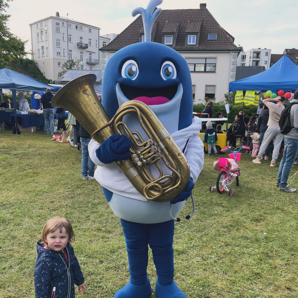 Maskottchen mit Tenorhorn und ein Kleinkind auf der Wiese beim Kids Day 2024