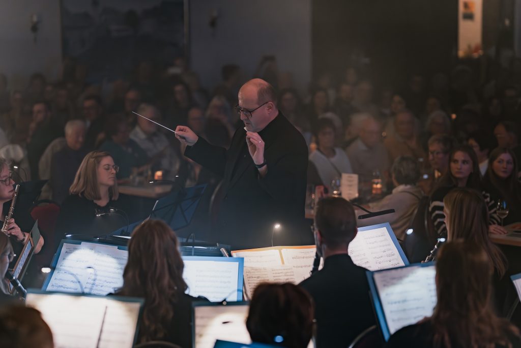 Der Dirigent vor dem Orchester, im Hintergrund das Publikum beim Herbstkonzert 2025